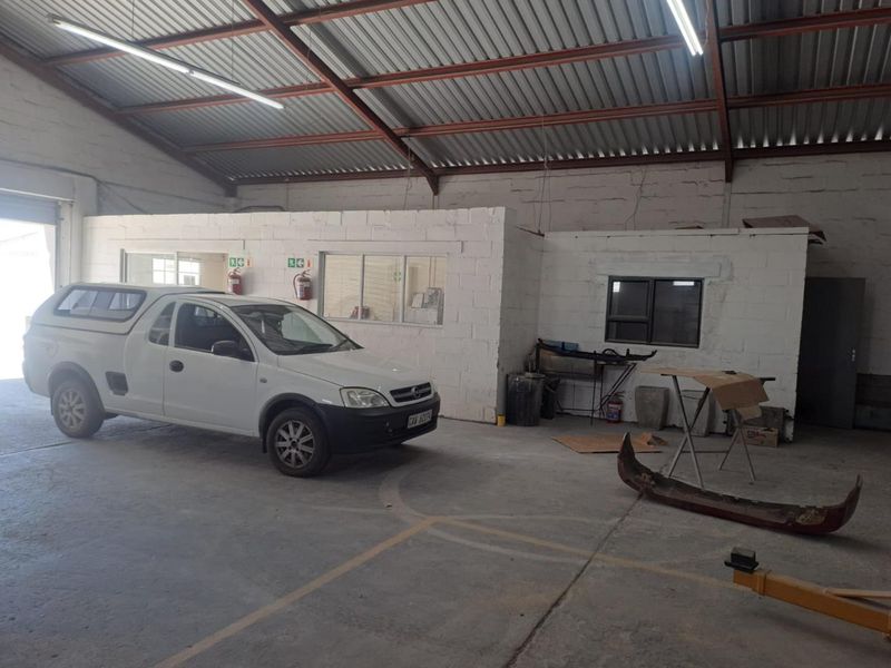 Spacious industrial garage featuring high corrugated metal ceilings, exposed steel trusses, concrete flooring, and an integrated internal office partition.