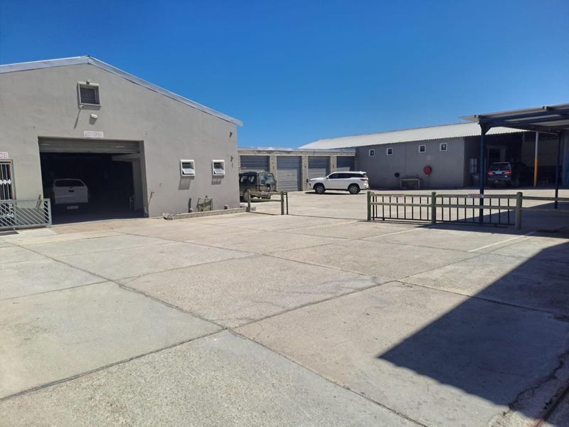 Spacious industrial yard featuring concrete paving, multiple roller shutter access points, and covered parking areas suitable for commercial operations.