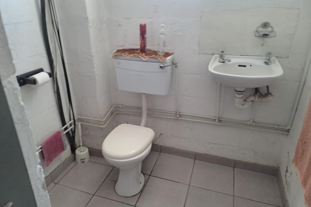 A basic industrial-style bathroom featuring a wall-mounted basin, toilet, and exposed plumbing with tiled flooring and unfinished block walls.