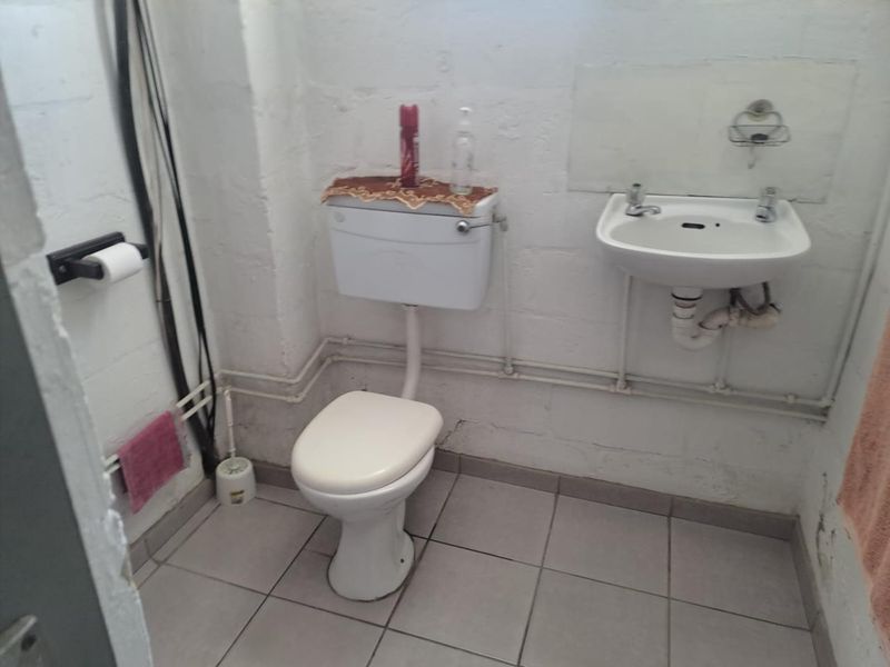 A basic industrial-style bathroom featuring a wall-mounted basin, toilet, and exposed plumbing with tiled flooring and unfinished block walls.