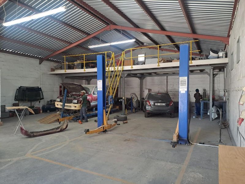 Industrial workshop space featuring a two-post vehicle lift, mezzanine storage level with safety railing, and exposed steel roof structure.