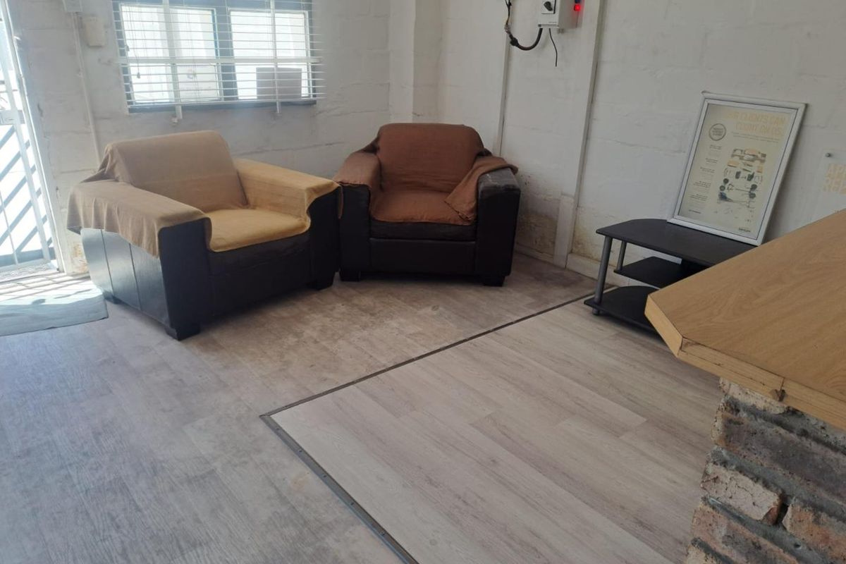 A functional industrial-style space featuring laminate flooring, exposed brick walls, and visible electrical infrastructure, suitable for a reception or waiting area.