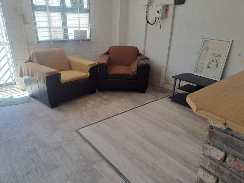 A functional industrial-style space featuring laminate flooring, exposed brick walls, and visible electrical infrastructure, suitable for a reception or waiting area.