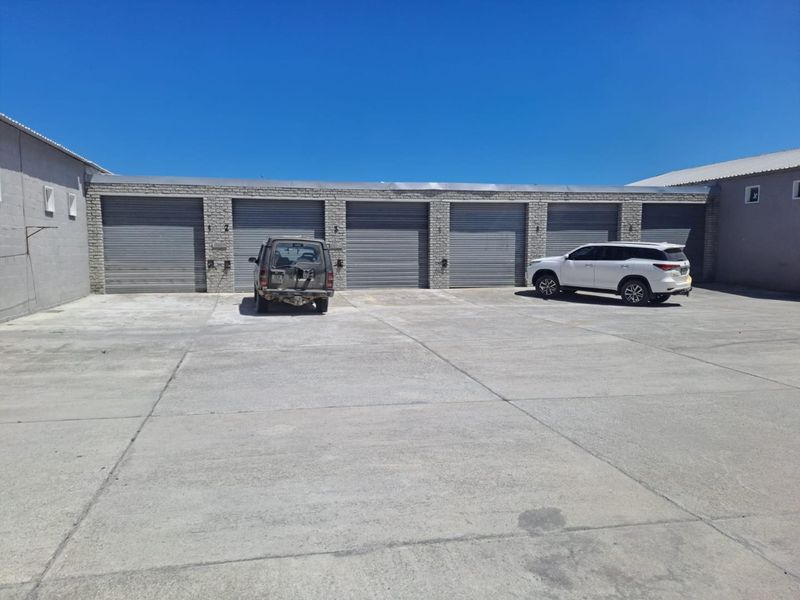 Industrial property featuring a row of secure roller shutter garage doors with a spacious concrete forecourt for vehicle access and parking.