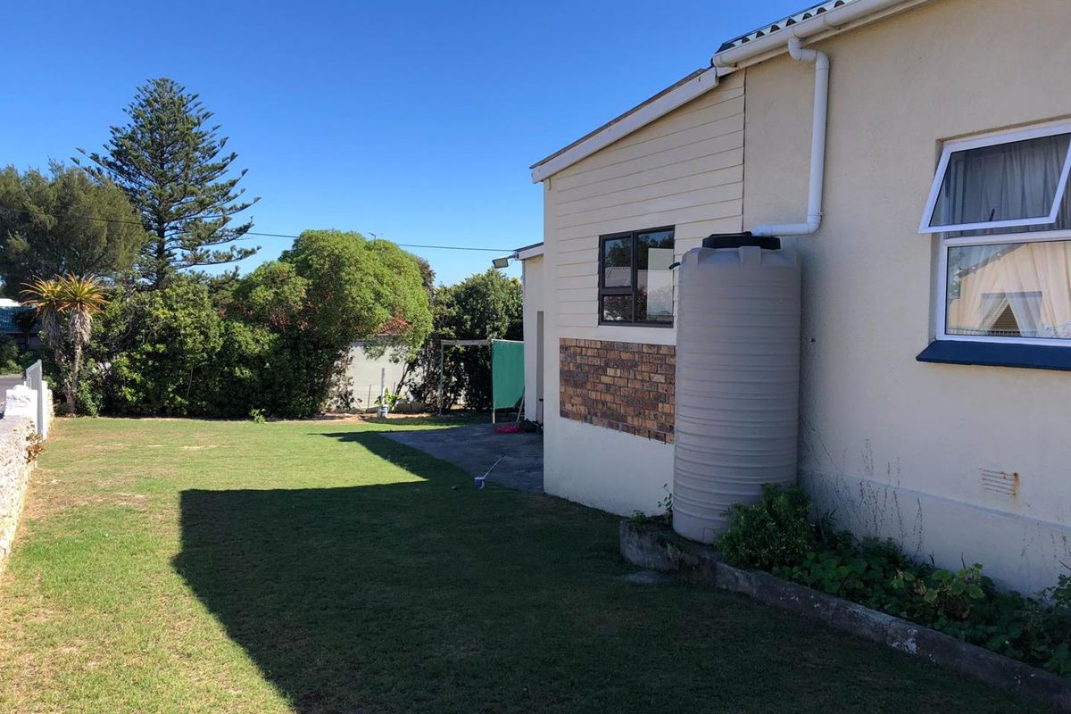 Rear exterior view of the property featuring a lawn, concrete patio area, and a fitted water tank connected to the gutter system.