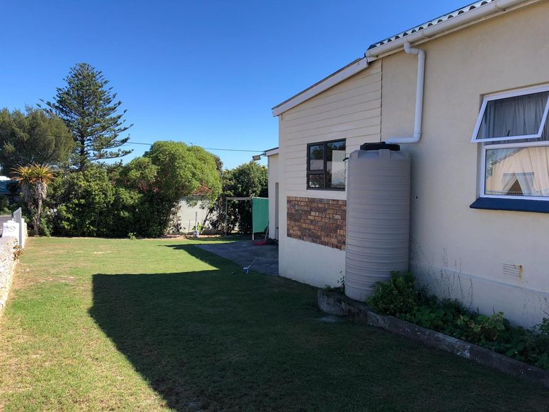 Rear exterior view of the property featuring a lawn, concrete patio area, and a fitted water tank connected to the gutter system.