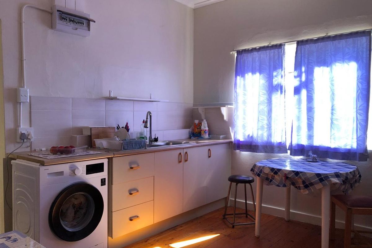 A functional kitchen area featuring timber flooring, built-in cabinetry, a stainless steel sink, and a tiled splashback with an exposed electrical distribution board.