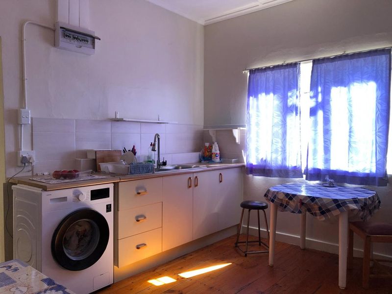 A functional kitchen area featuring timber flooring, built-in cabinetry, a stainless steel sink, and a tiled splashback with an exposed electrical distribution board.