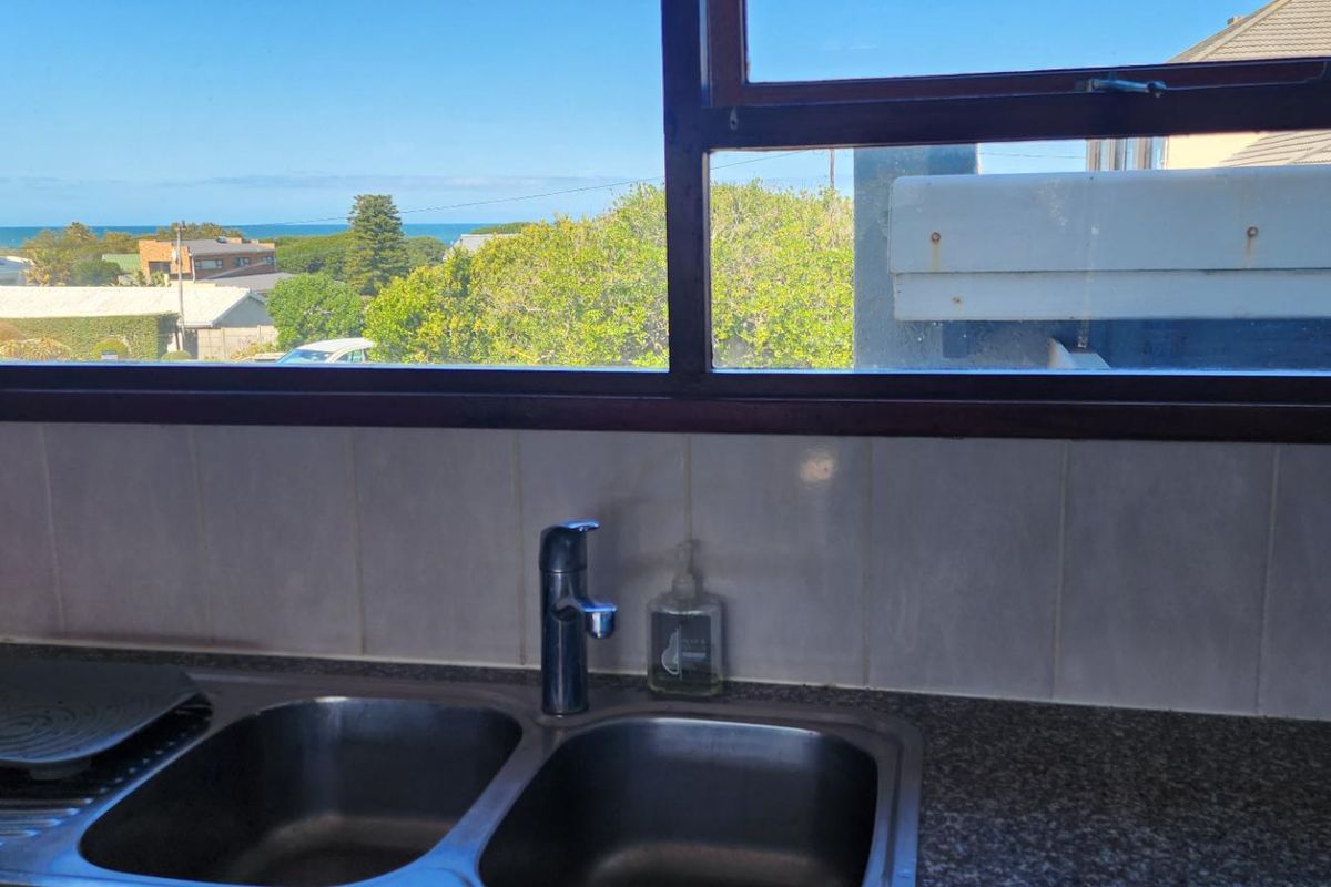 Kitchen sink area featuring a double stainless steel basin, granite countertop, and tiled splashback with a view of the surrounding neighborhood and ocean.