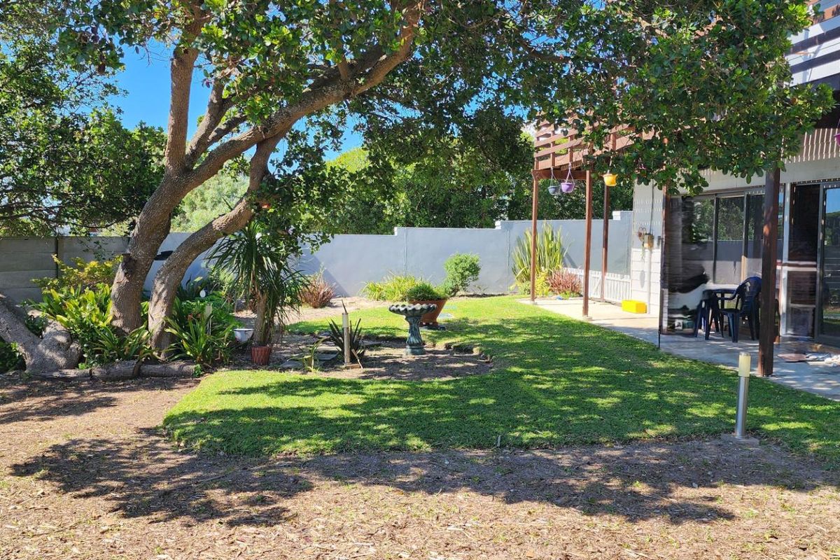 Rear garden featuring a lawn area, mature trees, concrete boundary wall, and a covered patio with an overhead wooden deck.