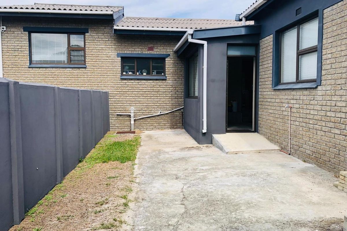 Rear exterior view of the property featuring a concrete patio area, brick facade, and a private boundary wall.