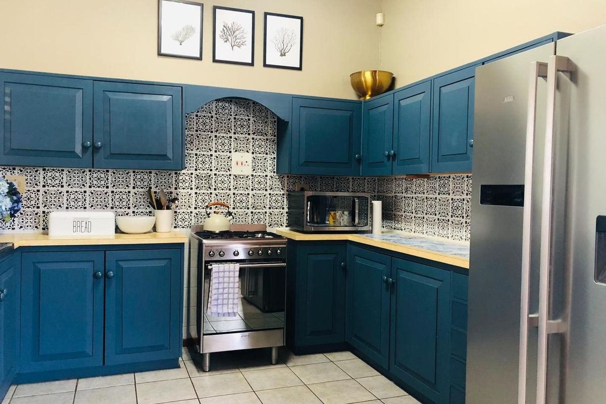 A well-maintained kitchen featuring blue cabinetry, patterned tile backsplash, wooden countertops, and a stainless steel gas stove.