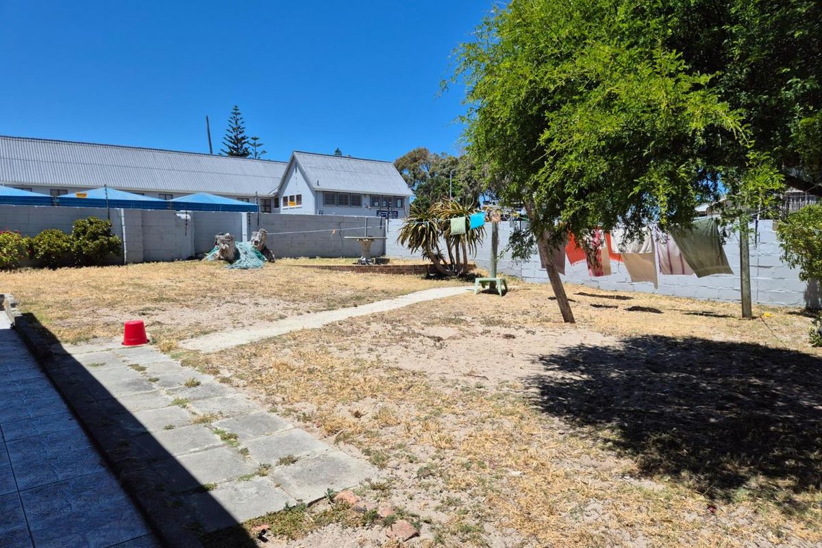 A spacious rear garden featuring a concrete block boundary wall, a paved walkway, and established trees, offering potential for landscaping improvements.
