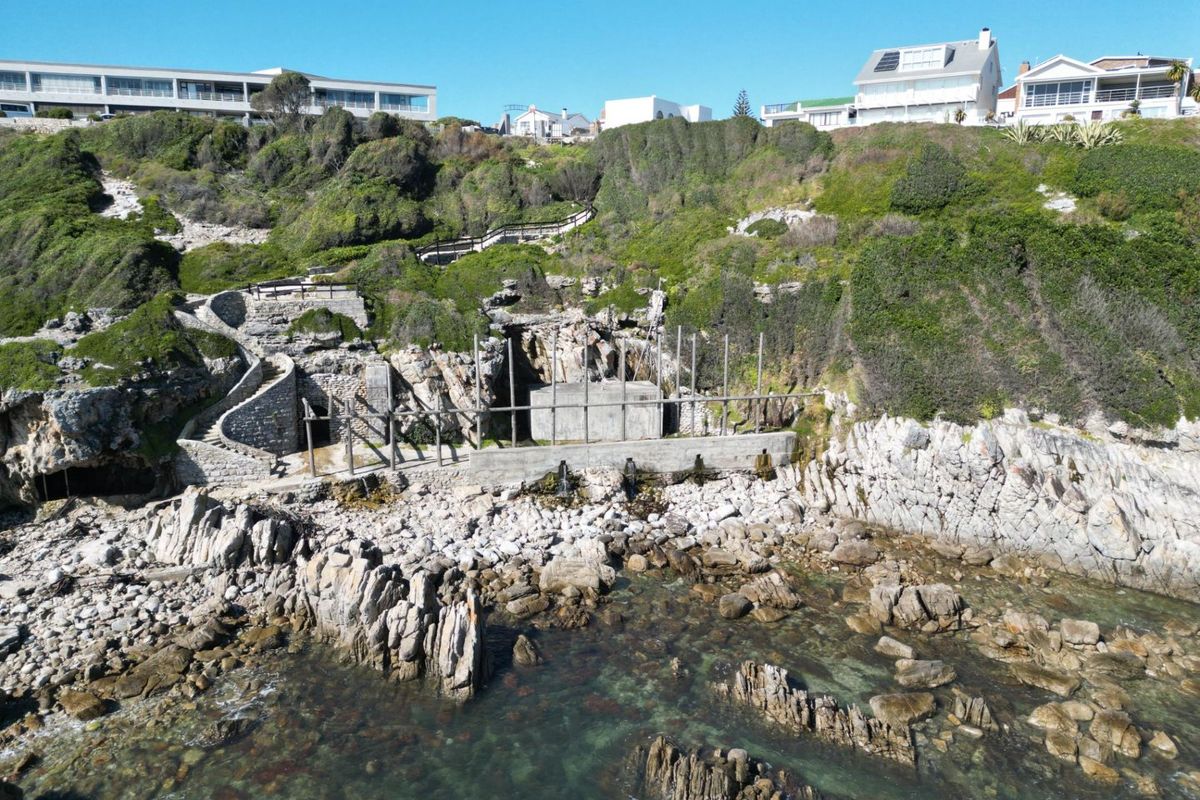 Aerial view of a coastal property featuring stone retaining walls, a concrete structure, and a stone staircase leading up the cliffside.