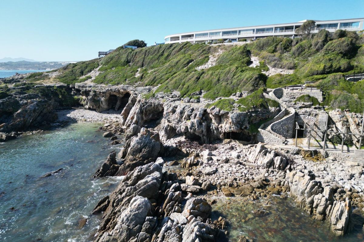 Aerial view of a rugged coastal landscape featuring natural rock formations, a stone staircase, and a cliffside setting overlooking the ocean.