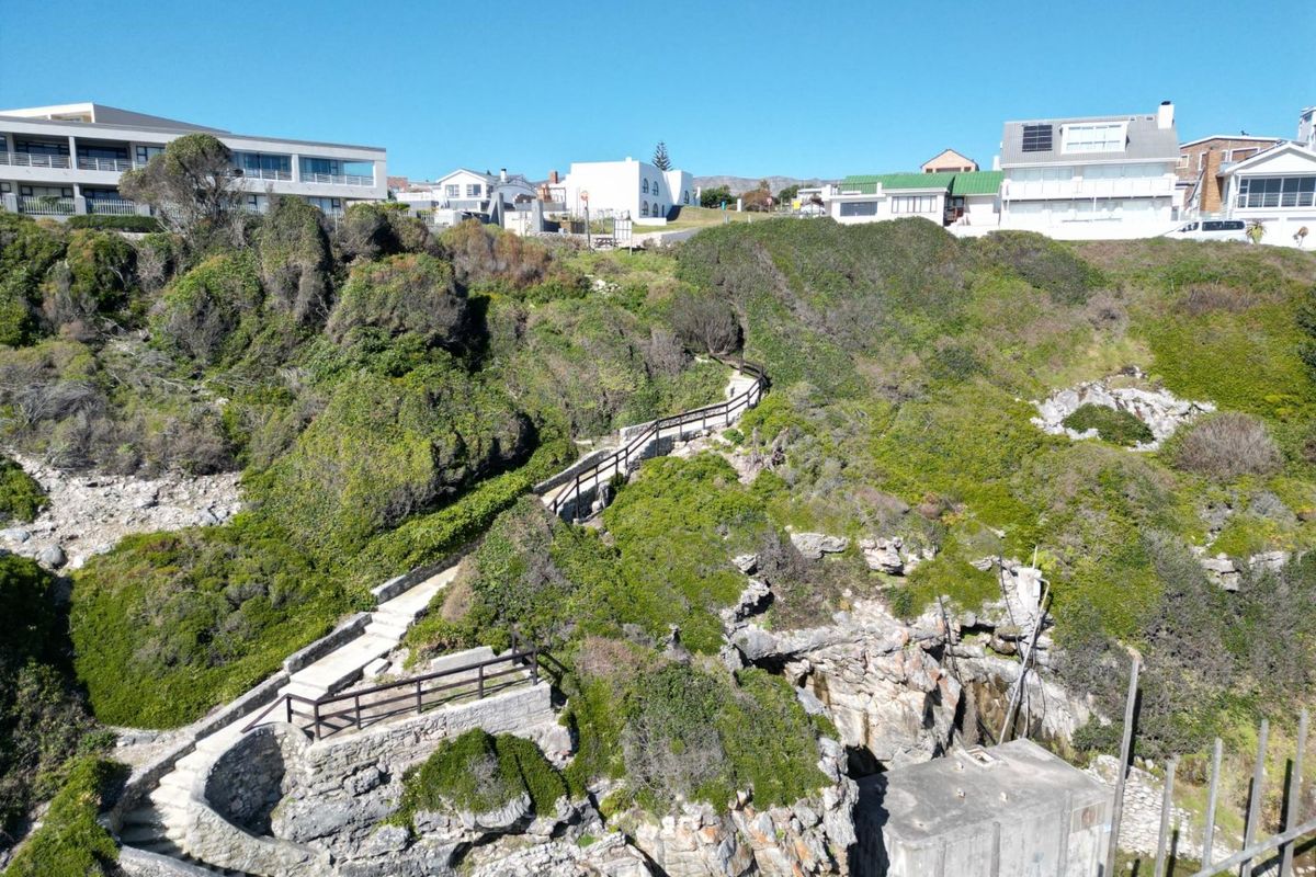 An elevated view of a coastal cliffside featuring a stone staircase with timber handrails leading down through natural vegetation.