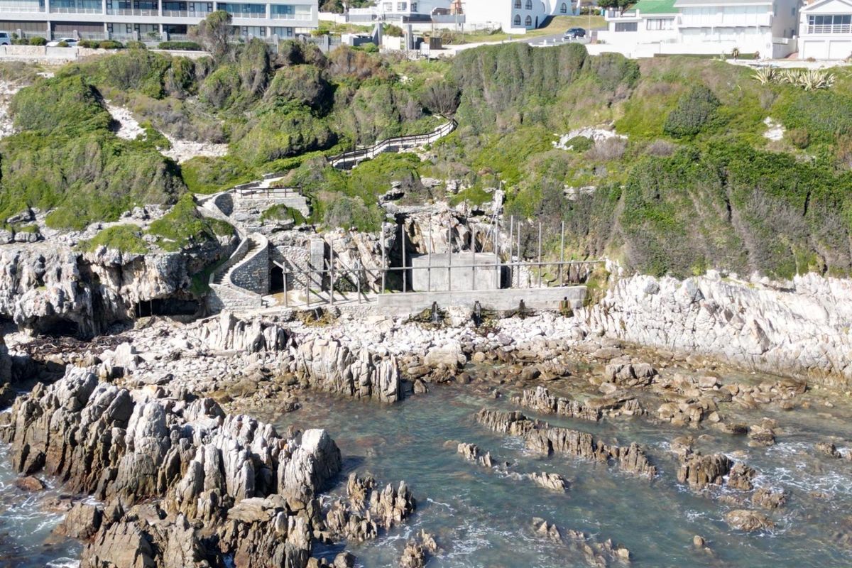 Aerial view of a coastal residential plot featuring rugged rock formations, a stone staircase, and existing concrete retaining structures along the shoreline.