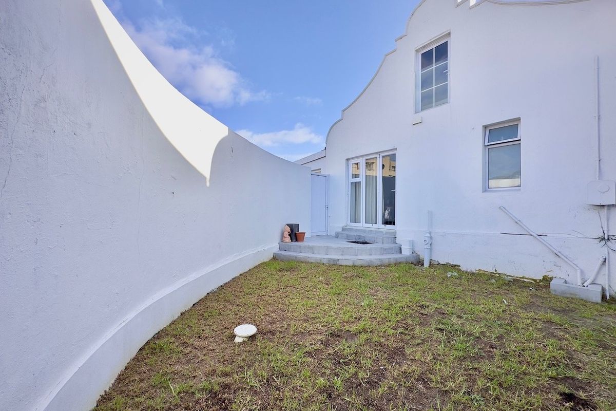 A rear exterior view featuring a private courtyard with a curved boundary wall, small lawn area, and direct access to the building via sliding doors.