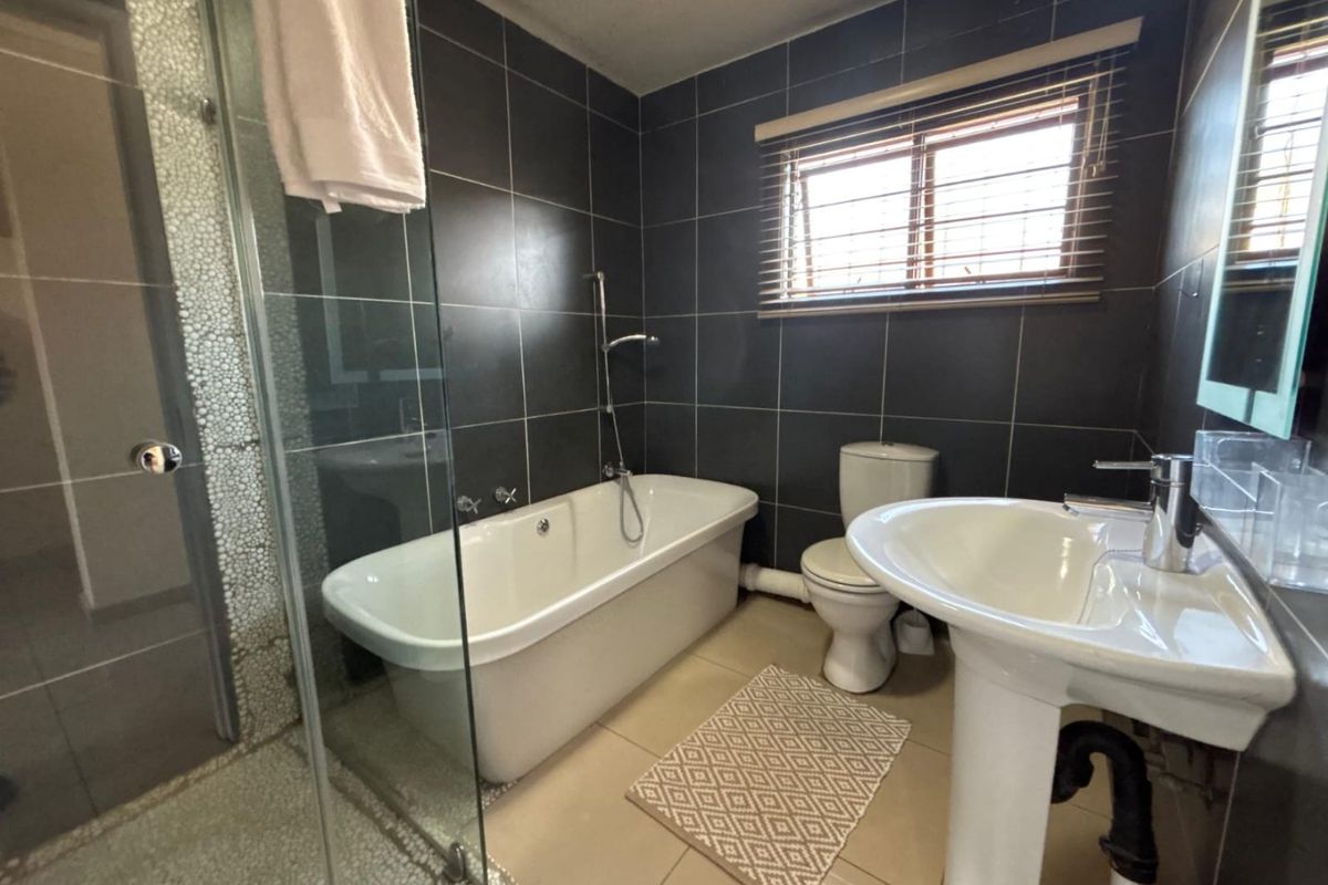A functional bathroom featuring a freestanding bathtub, separate glass shower enclosure, pedestal sink, and dark tiled walls.