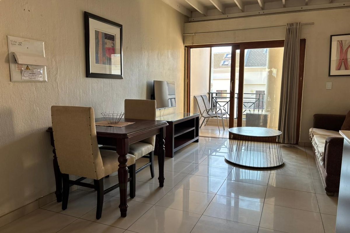 Open-plan living and dining area featuring tiled floors, exposed beam ceilings, and direct access to a private balcony through sliding glass doors.