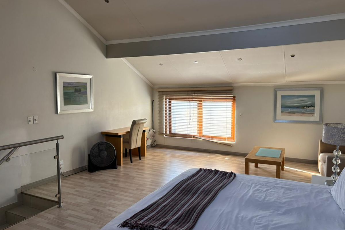 Spacious bedroom featuring a sloped ceiling, recessed lighting, laminate flooring, and a staircase with a modern glass and stainless steel balustrade.