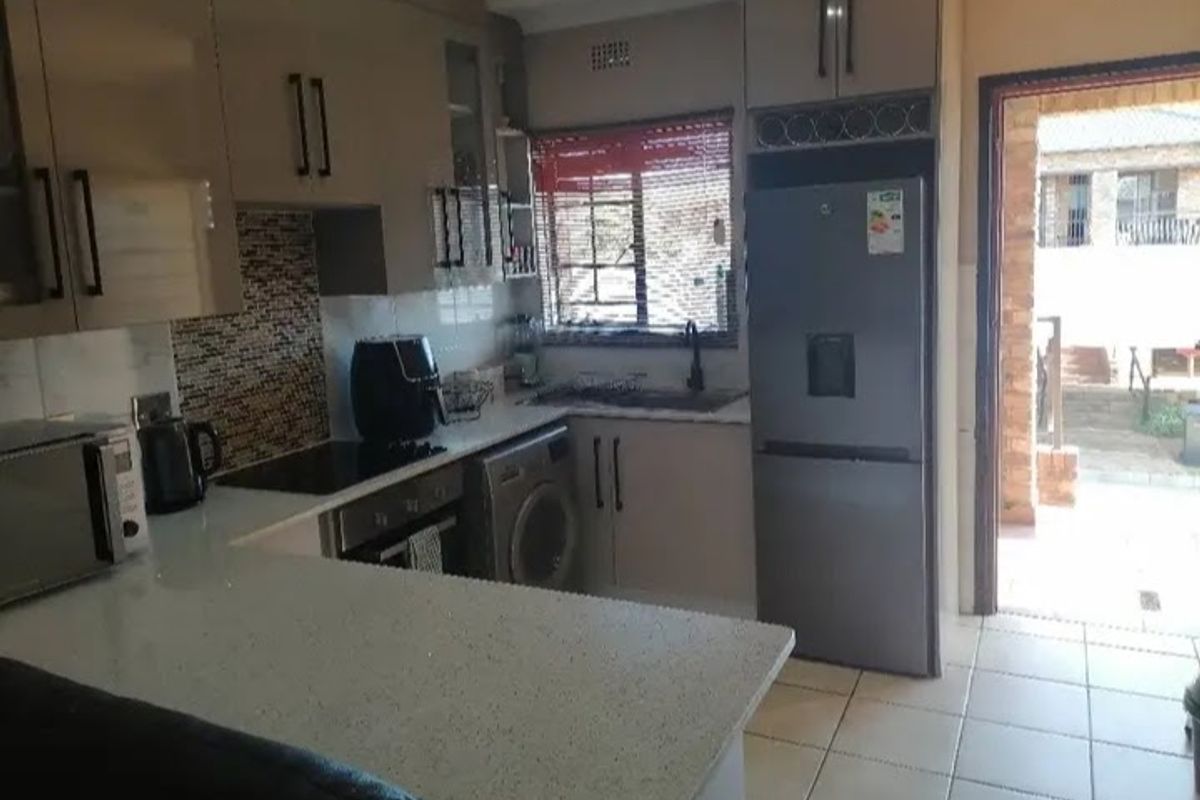 A functional kitchen featuring modern cabinetry, stone countertops, a mosaic tile backsplash, and integrated laundry facilities with direct access to an outdoor area.