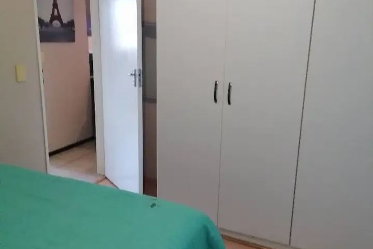 A bedroom featuring built-in wardrobes and laminate flooring, with an open doorway leading to an adjacent room.