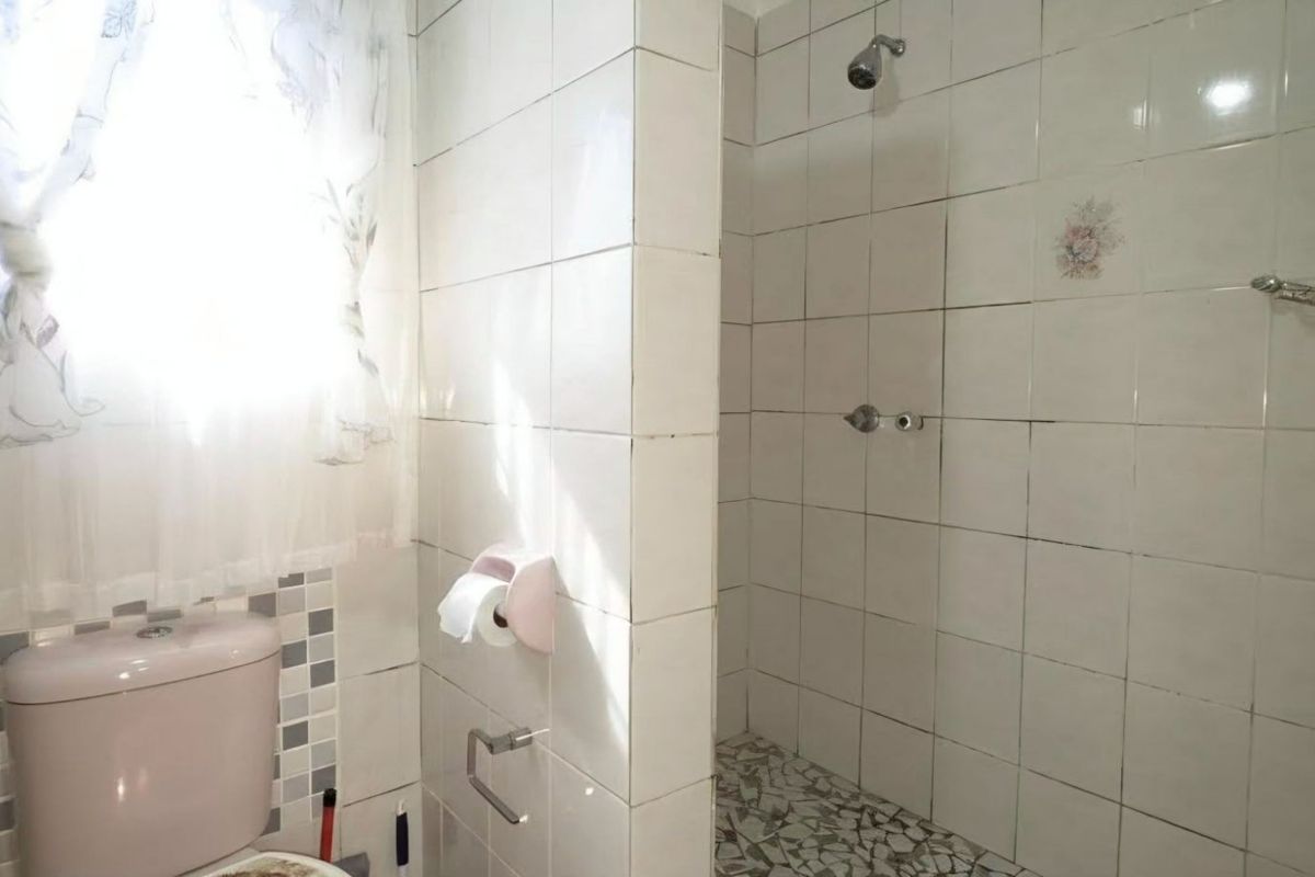 A functional bathroom featuring a shower enclosure with tiled walls and a standard toilet, requiring cosmetic updates to modernize the space.
