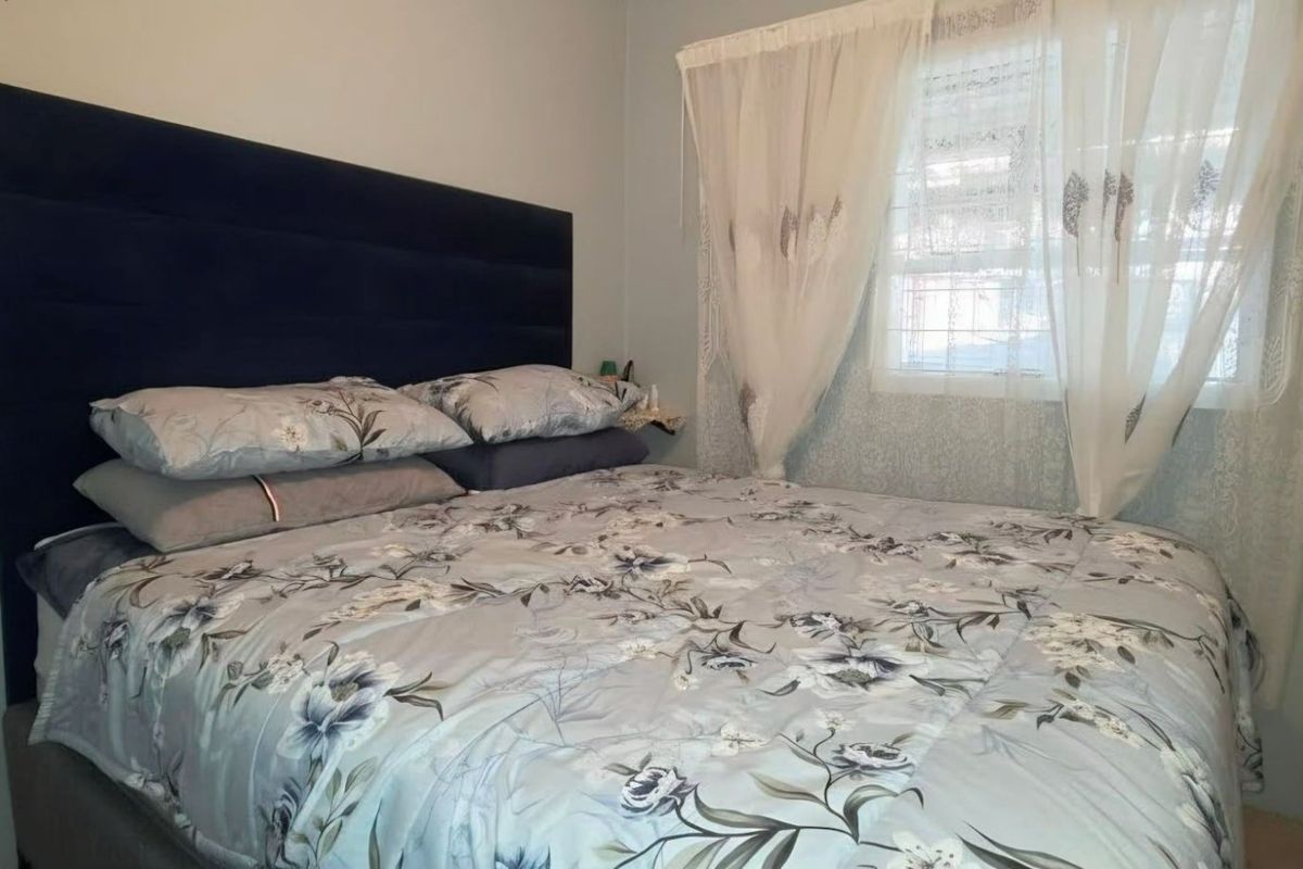 A bedroom featuring a window with curtains and a wall-mounted electrical outlet.
