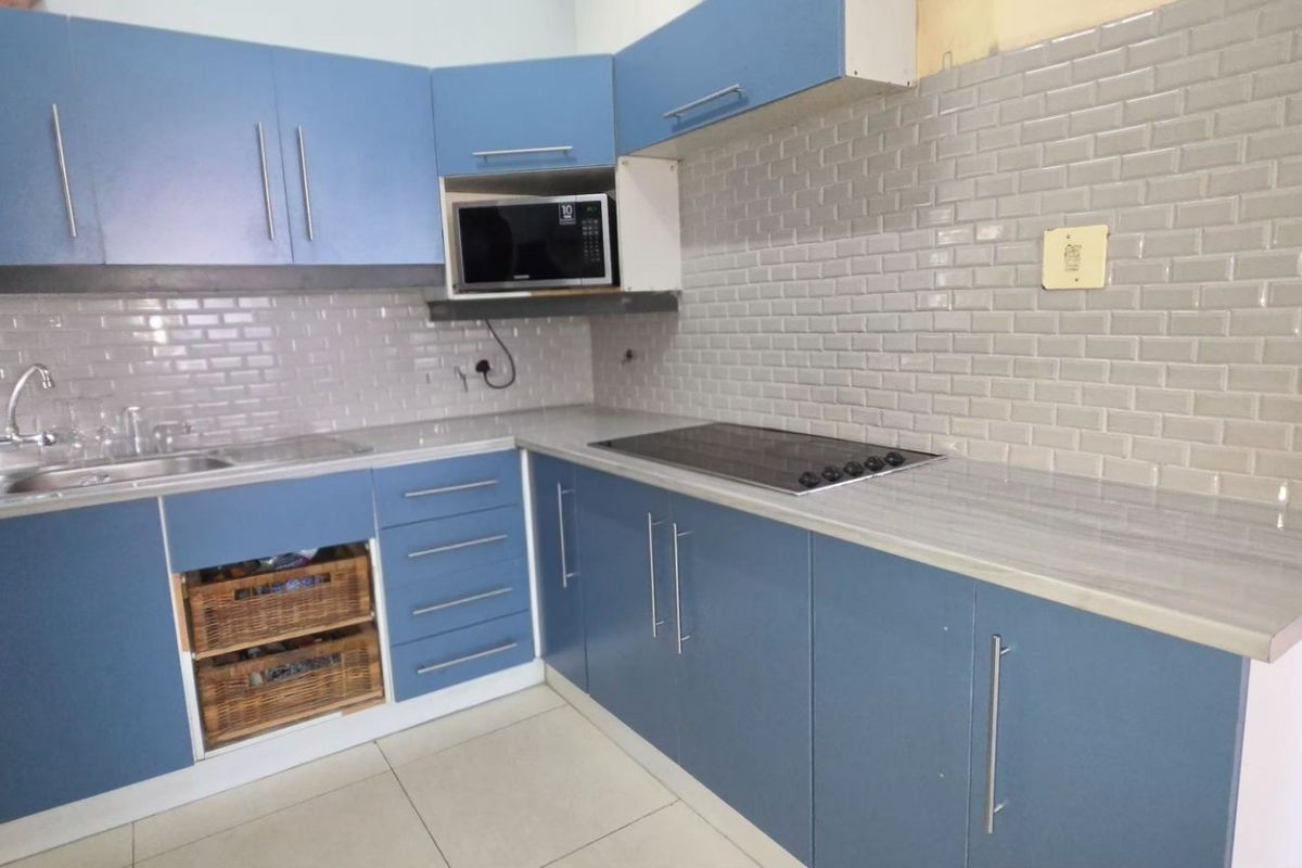 A functional kitchen featuring blue cabinetry, subway tile backsplash, laminate countertops, and integrated appliances, with some minor finishing work required above the upper cabinets.