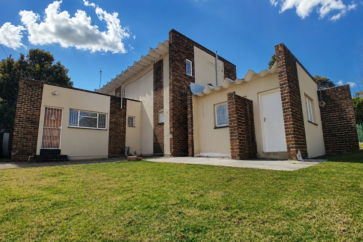 Rear view of the house featuring a brick and plaster facade, corrugated roofing, and a concrete patio area overlooking the garden.