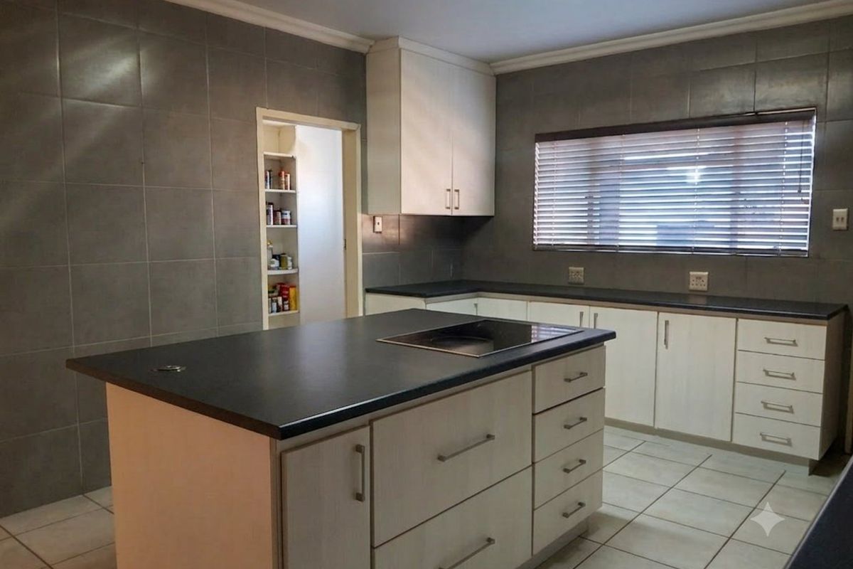 A functional kitchen featuring a central island with a built-in hob, ample cabinetry, tiled walls, and an adjacent walk-in pantry.
