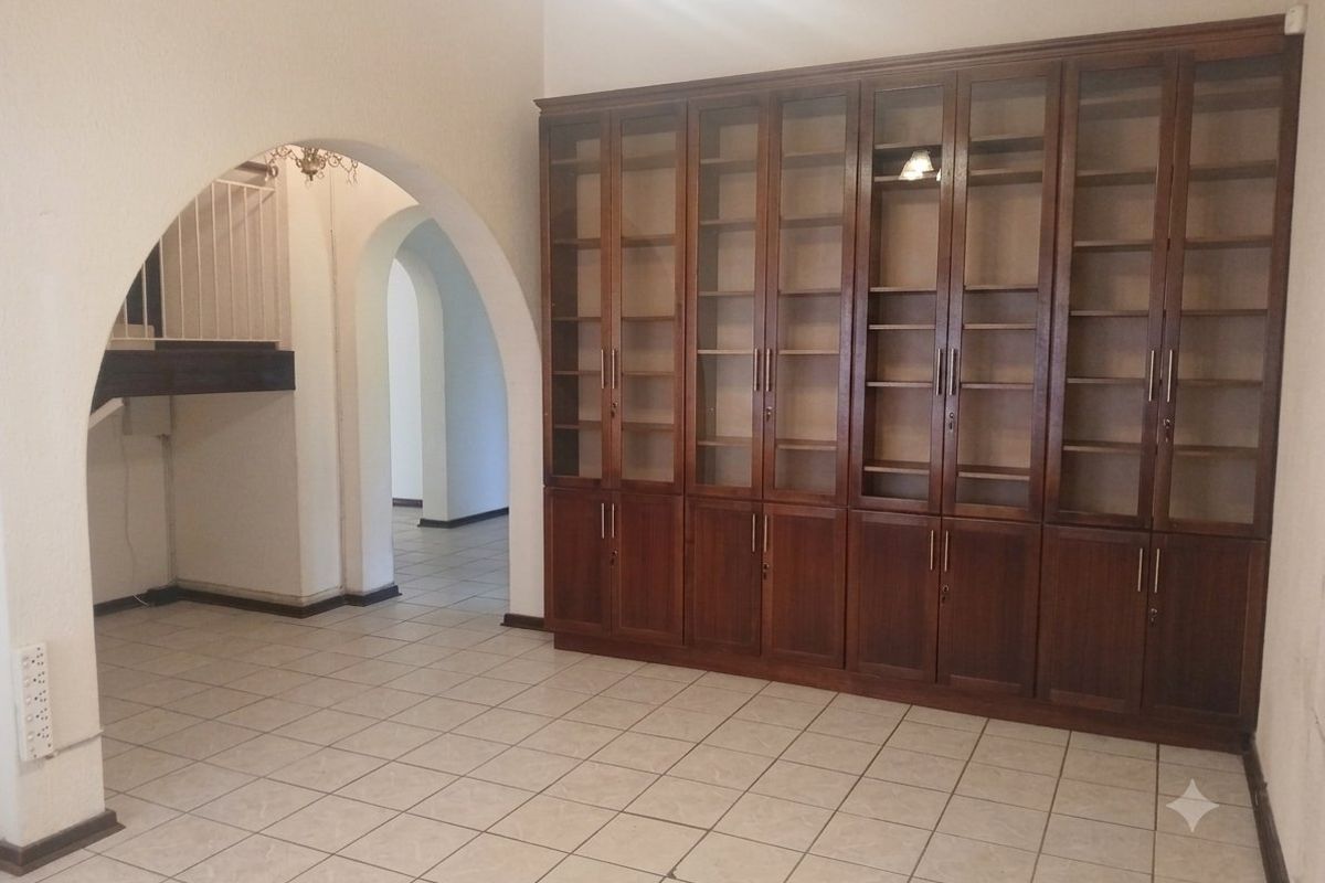 Spacious living area featuring large built-in wooden display cabinetry, classic archways, and neutral tiled flooring throughout.