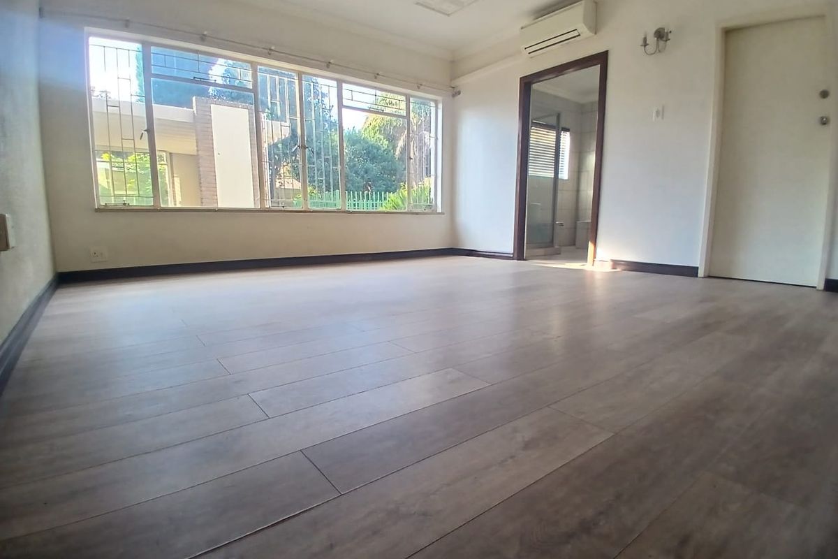 Spacious, empty bedroom featuring modern laminate flooring, a wall-mounted air conditioning unit, and large windows with security bars.
