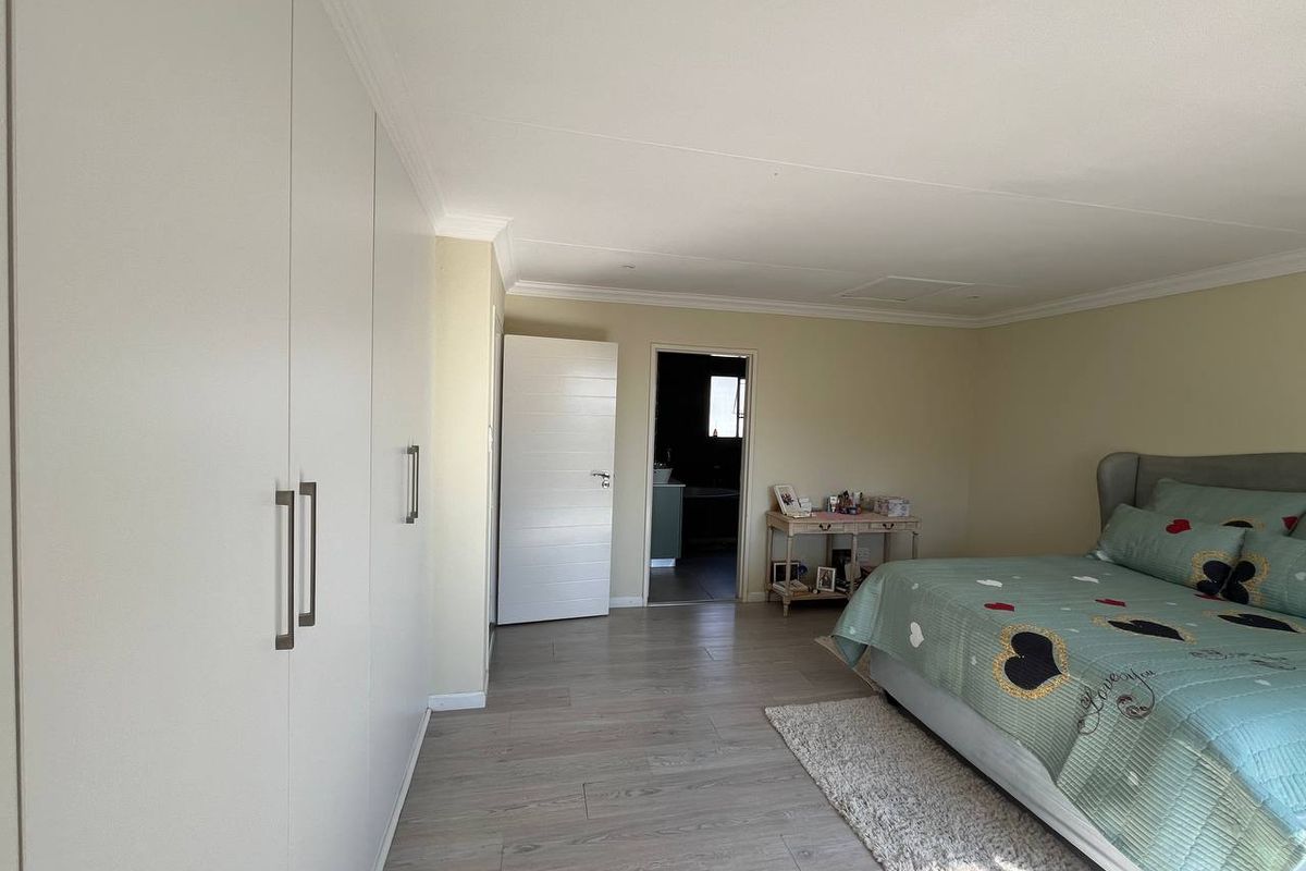 A spacious bedroom featuring light-toned laminate flooring, extensive built-in cupboards, and direct access to an adjoining bathroom.
