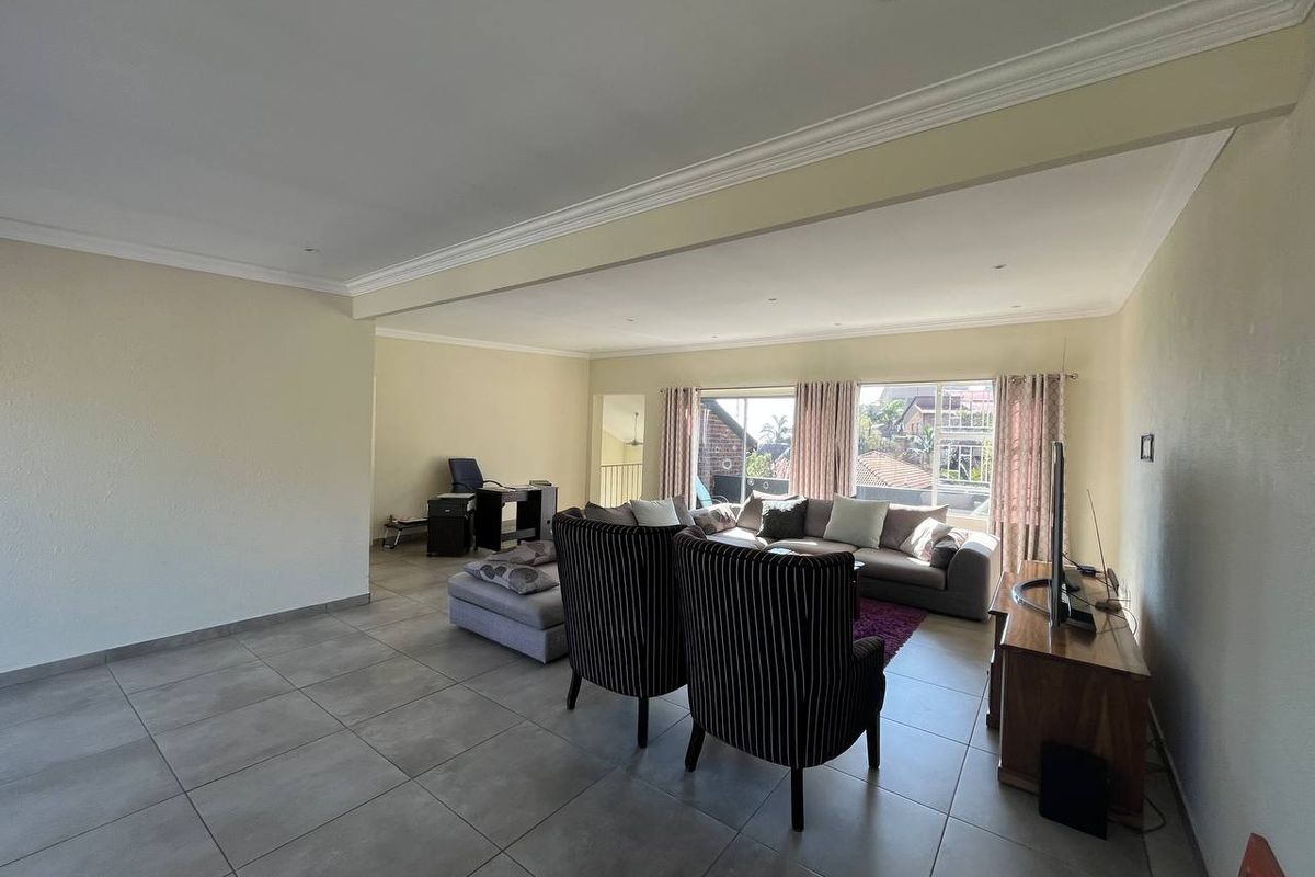 Spacious open-plan living area featuring large windows, neutral tiled flooring, and recessed downlighting, offering a bright and versatile space for relaxation.