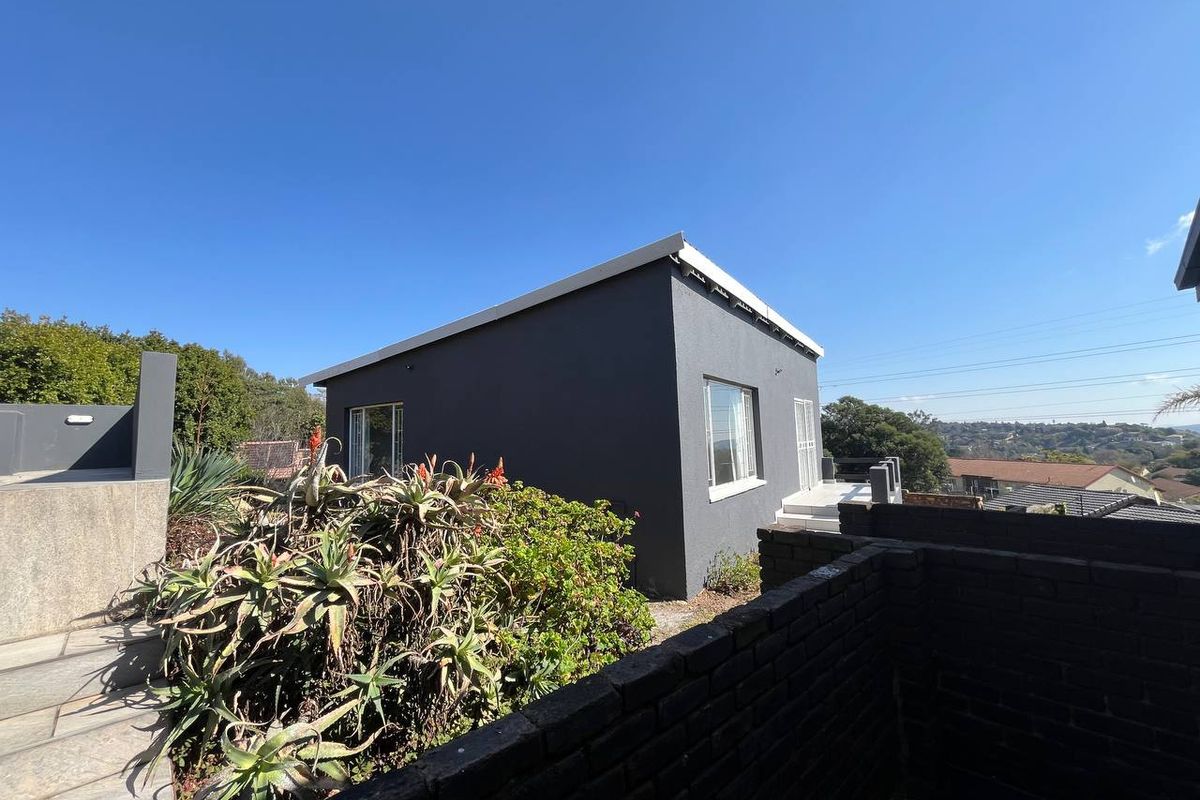 Rear view of the property featuring a dark grey exterior finish, paved walkway, and established garden area with a brick boundary wall.