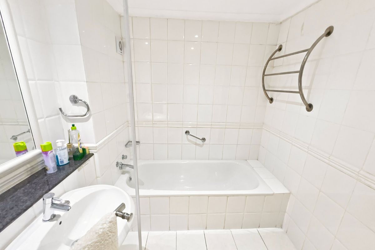 A functional bathroom featuring a built-in bathtub, wall-mounted basin, chrome fixtures, and a heated towel rail, finished with white wall and floor tiles.