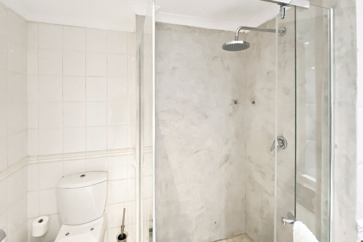 A clean, modern bathroom featuring a glass-enclosed shower with a rain shower head, cement-look wall finishes, and white tiled walls.