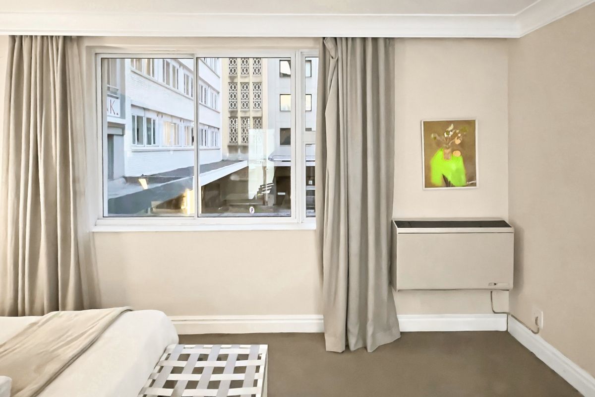 A well-maintained bedroom featuring neutral wall tones, a sliding window with curtains, and a wall-mounted air conditioning unit.