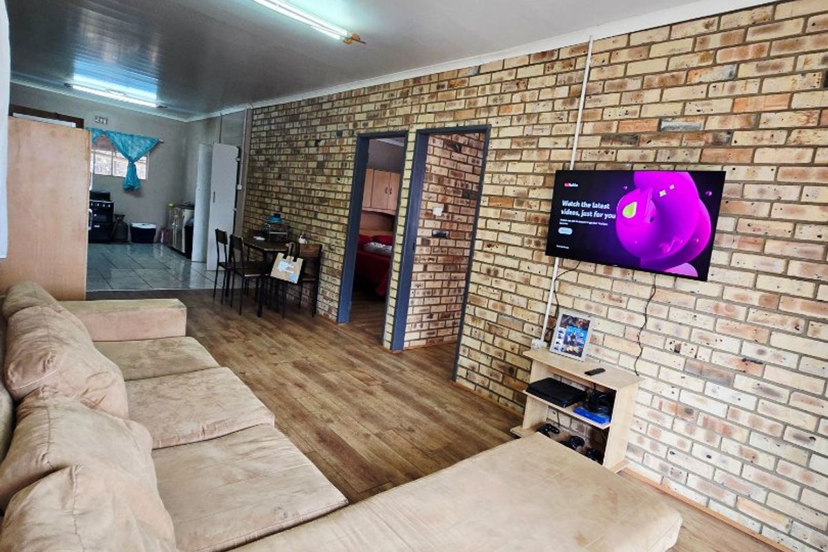 Living room featuring an exposed brick feature wall, laminate flooring, and direct access to the adjacent kitchen and dining area.