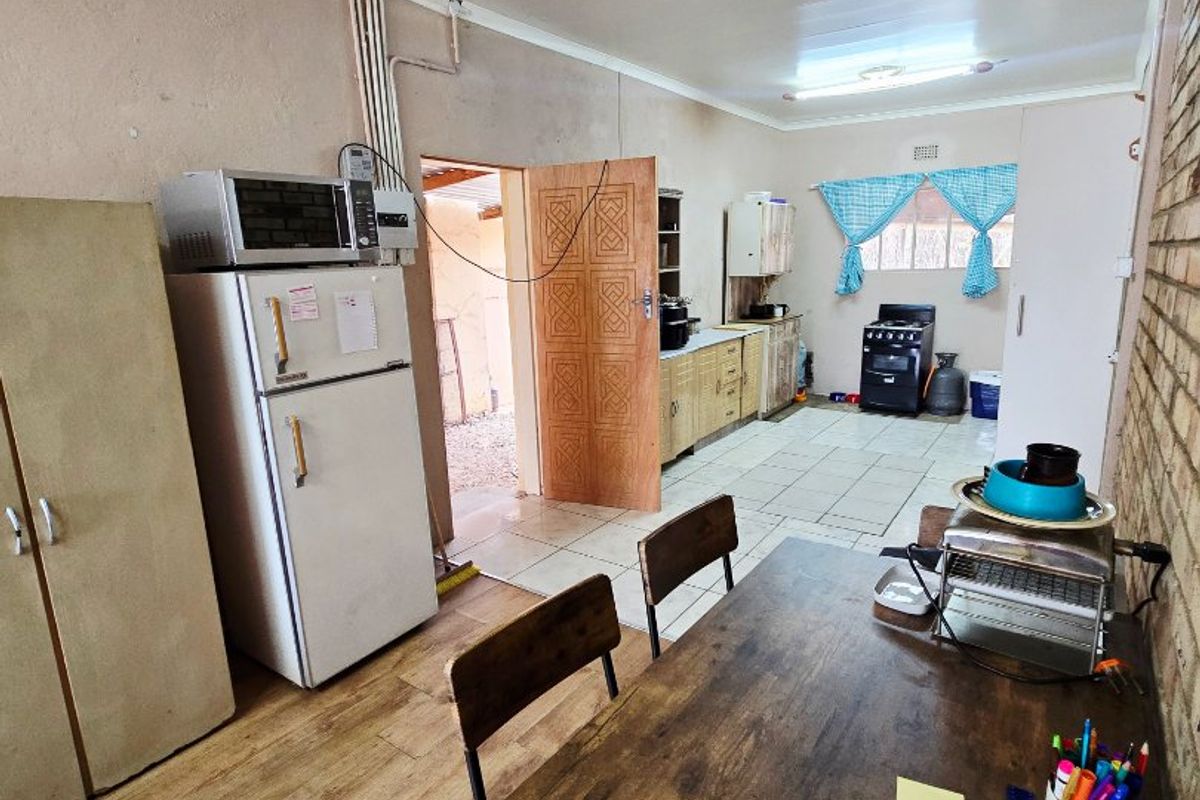 A functional kitchen area featuring a mix of tiled and laminate flooring, built-in cabinetry, and an exposed brick feature wall.