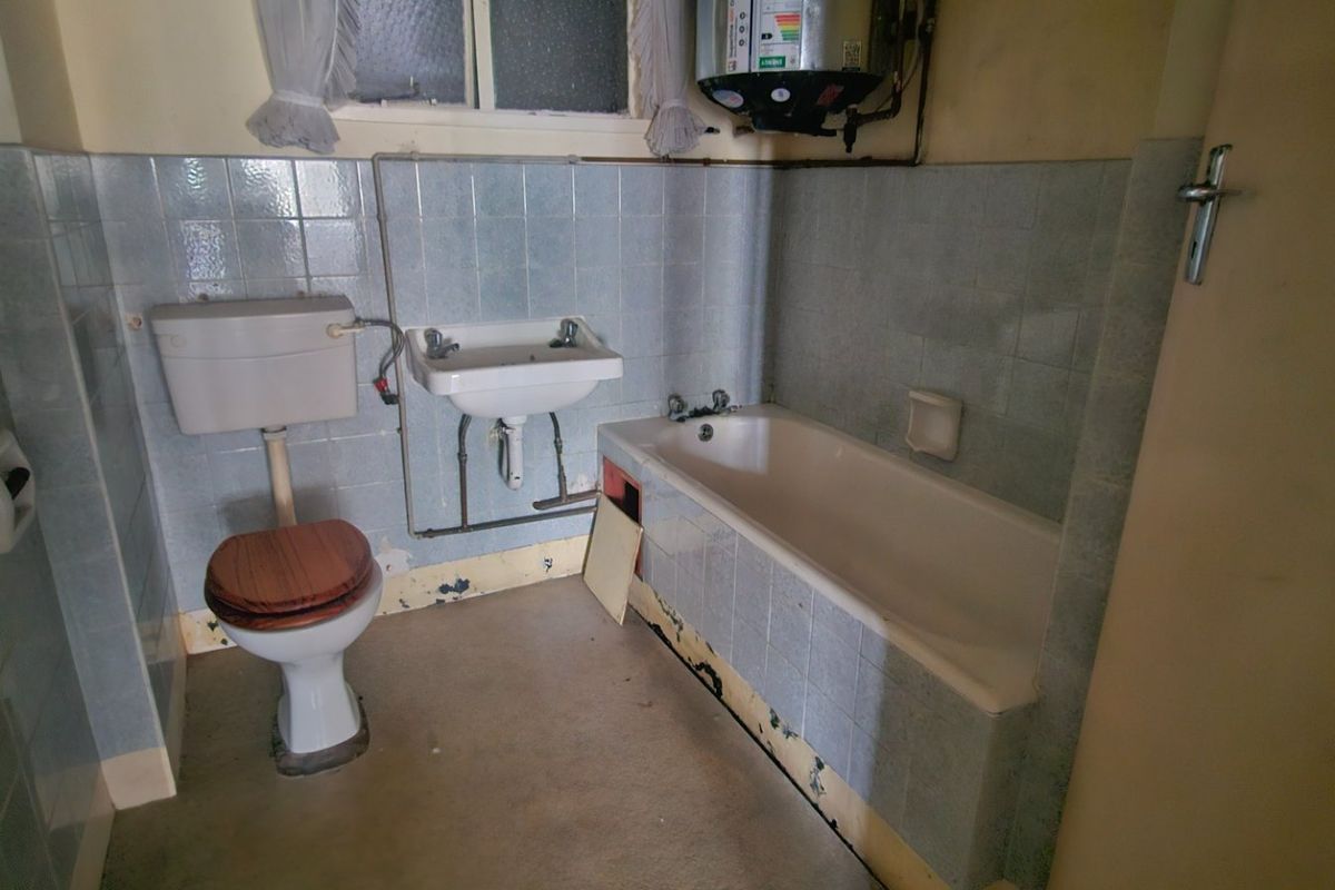 A dated bathroom featuring a bathtub, wall-mounted basin, and toilet, requiring renovation to update the finishes and address visible wear.