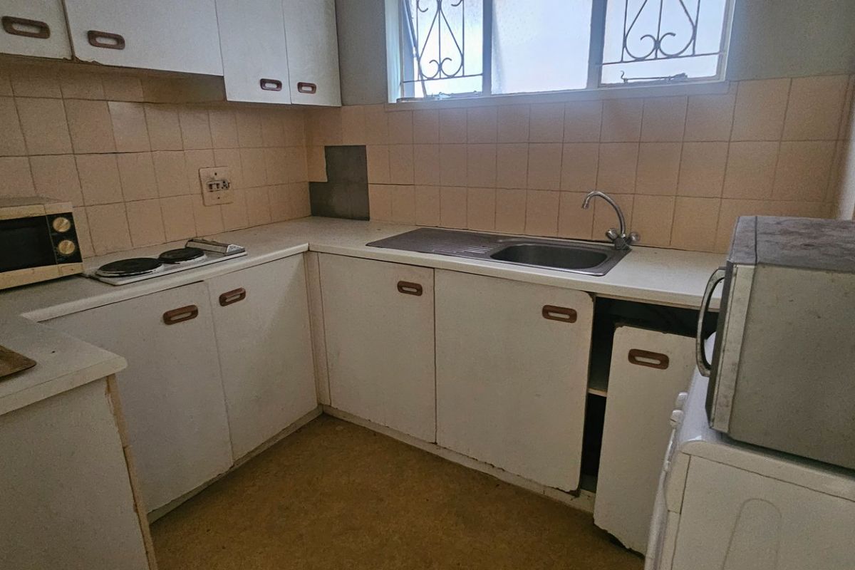 A dated kitchen featuring original laminate cabinetry, a stainless steel sink, and tiled backsplash, requiring modernization to improve functionality and aesthetic appeal.