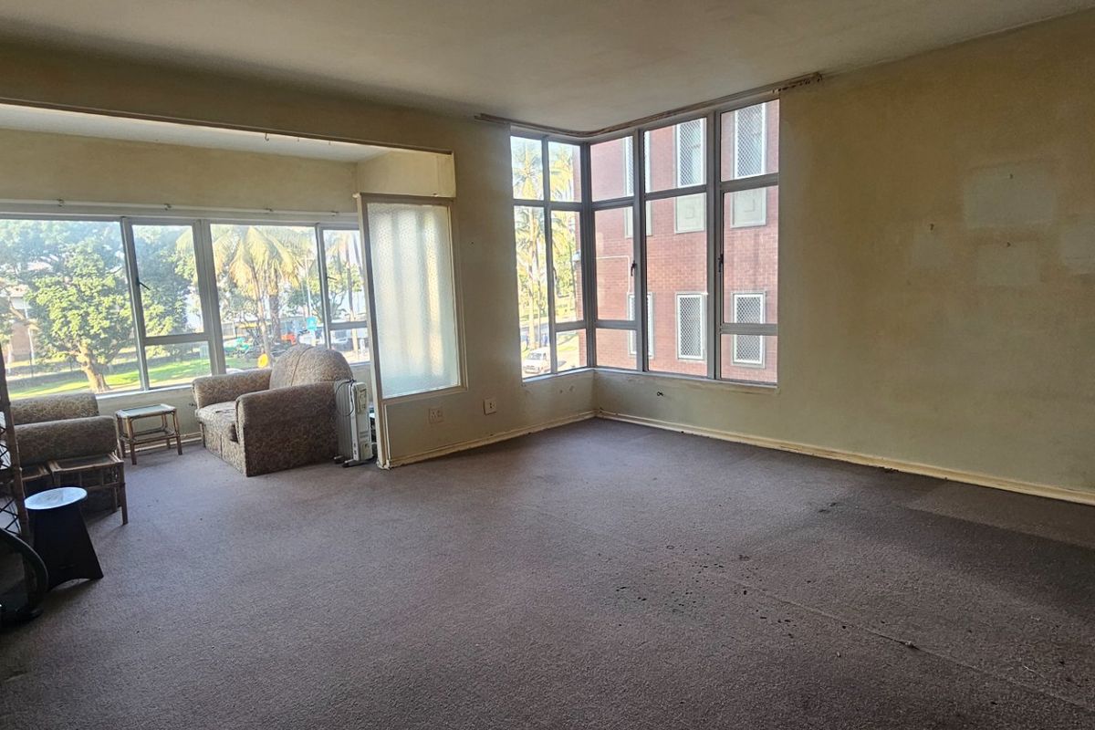 Spacious living area featuring large windows that provide ample natural light, requiring cosmetic updates to the flooring and wall finishes.