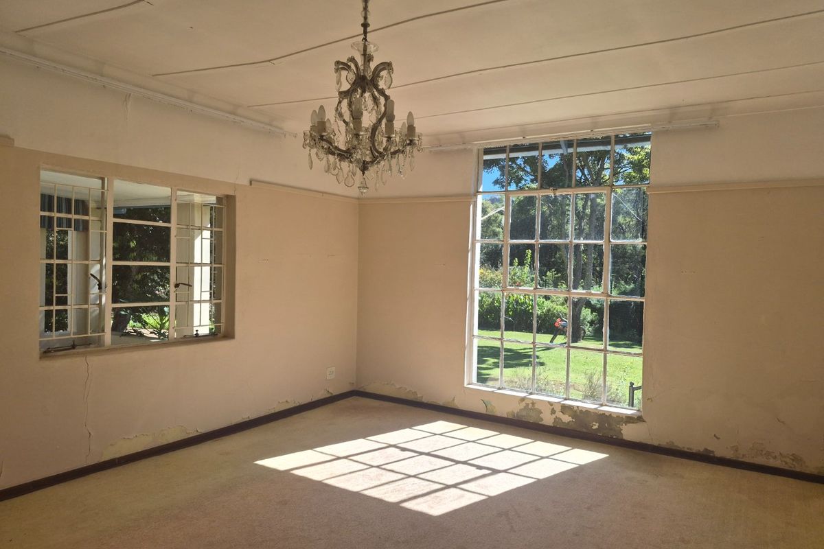 An empty living room featuring large steel-framed windows and a classic chandelier, requiring cosmetic updates to the walls and flooring.