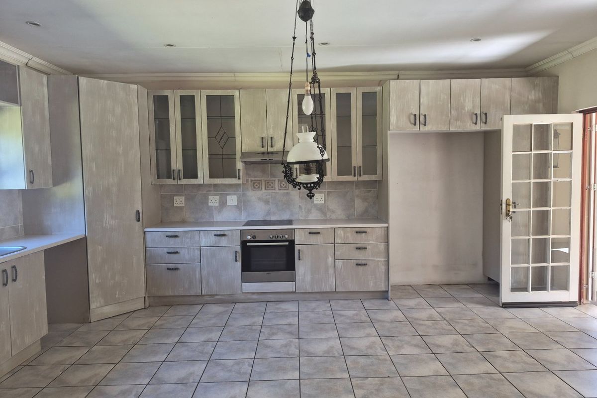 Spacious kitchen featuring built-in cabinetry, integrated oven and hob, tiled flooring, and direct access to the exterior via a glass-paneled door.
