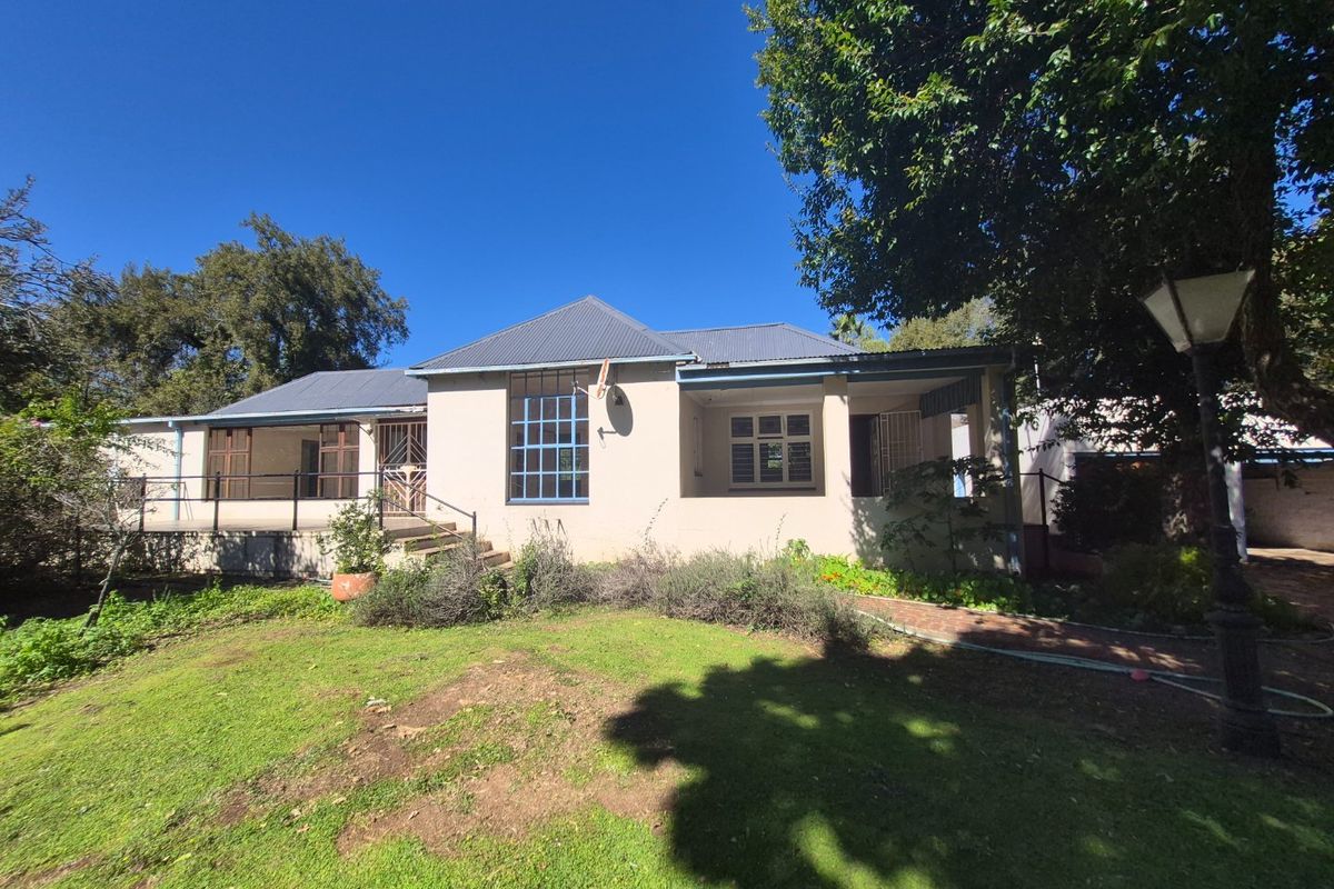Rear view of the farmhouse featuring a covered patio, metal roofing, and established garden surroundings.