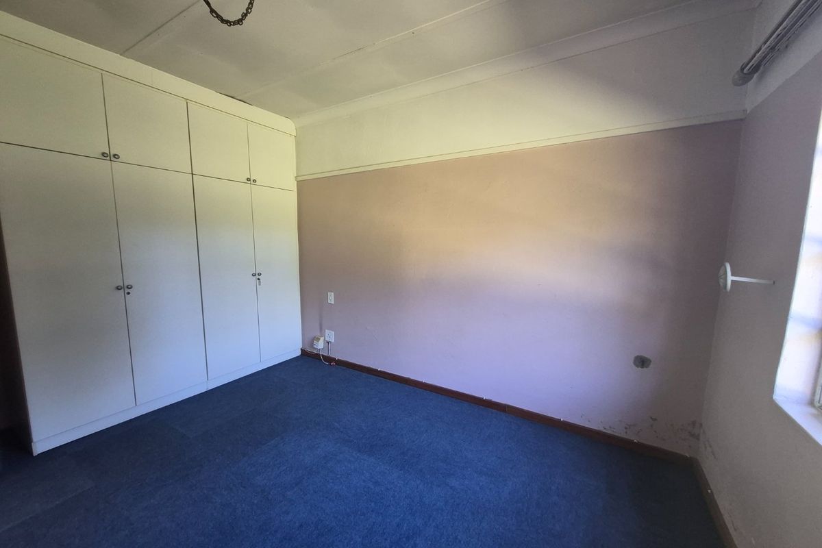 An empty bedroom featuring built-in cupboards, carpeted flooring, and coved ceilings, requiring cosmetic updates to the wall finishes.