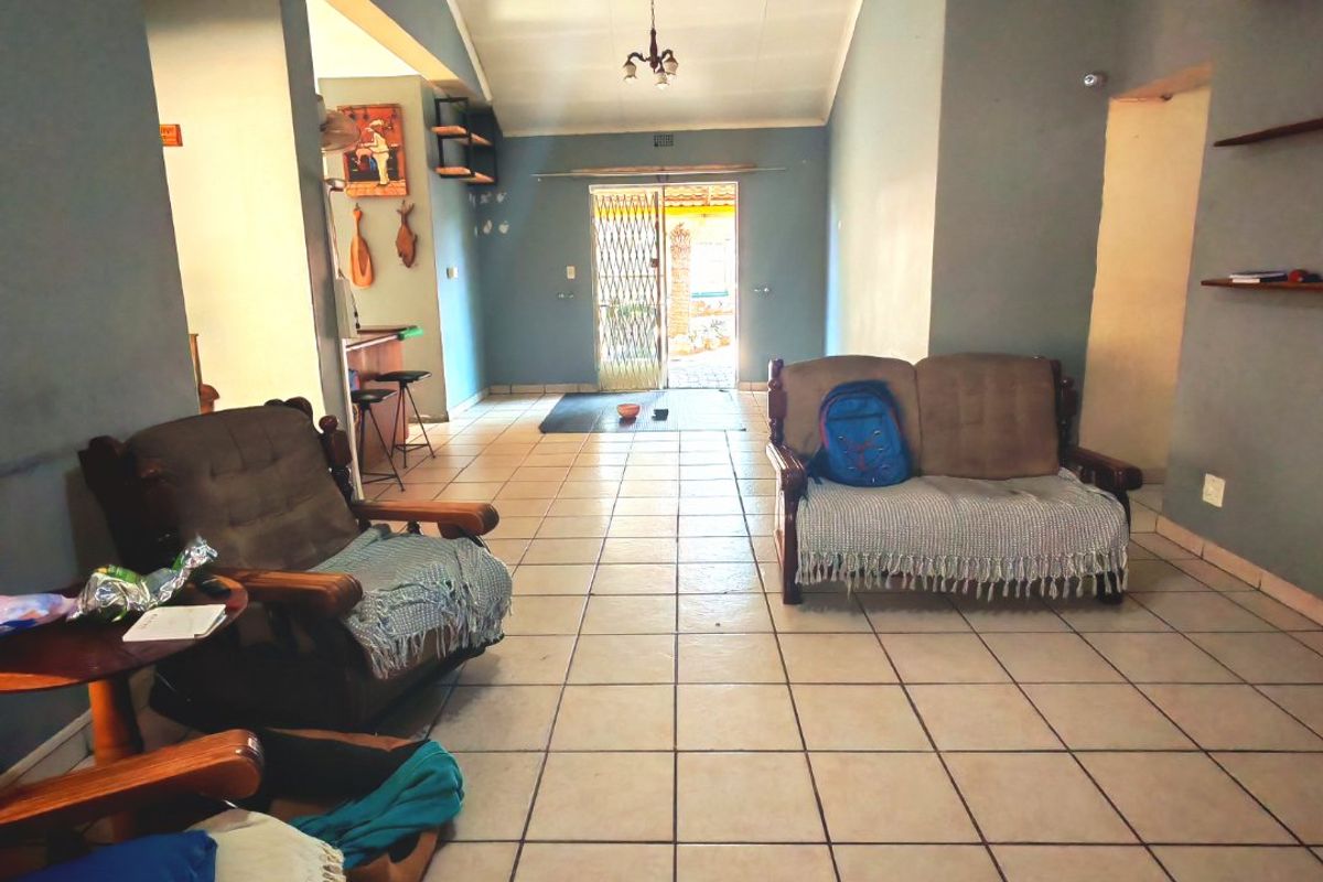 A spacious living area featuring ceramic floor tiles, a vaulted ceiling, and built-in wall shelving, leading to an exterior security gate.